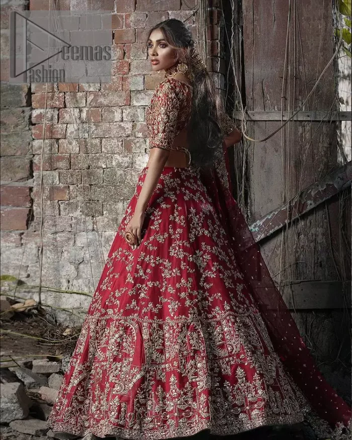 Envelop yourself into the dazzling love affair. Surprise everyone with this deep red article on your Big day. Stating this article with a deep red blouse that is handsomely styled with boat shape neckline. The half sleeves of the blouse just boost the attractiveness of the design.  In addition to this, it is delightfully furnished with golden embroidery which includes kora, dabka and tilla. Brace the blouse with a deep red fluffy lehenga that is again heavily embellished with golden embroidery that increases the beauty of the article. Complete this article with the same colour dupatta which is embellished with a four-sided borders and sequins sprayed all over just to envelop you into the dazzling love affair on your big day. 