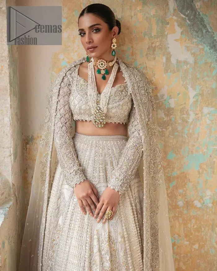 With a touch of Divine. A stunning ivory blouse is laboriously frosted with meticulously detailed hand embellishment with kora, dabka, tilla and pearls all over. The sweetheart neckline of the blouse and full sleeves together gives a so romantic look to any bride. In addition to this, it is systemized with the same colour frilled lehenga which is laden with the same colour embroidery that gives a magical stream of tilla, dabka and pearls. Finish this ivory article with the same colour dupatta that is heavily embellished with four-sided handsome borders and sequins sprayed all over to enhance the feeling of joy. 