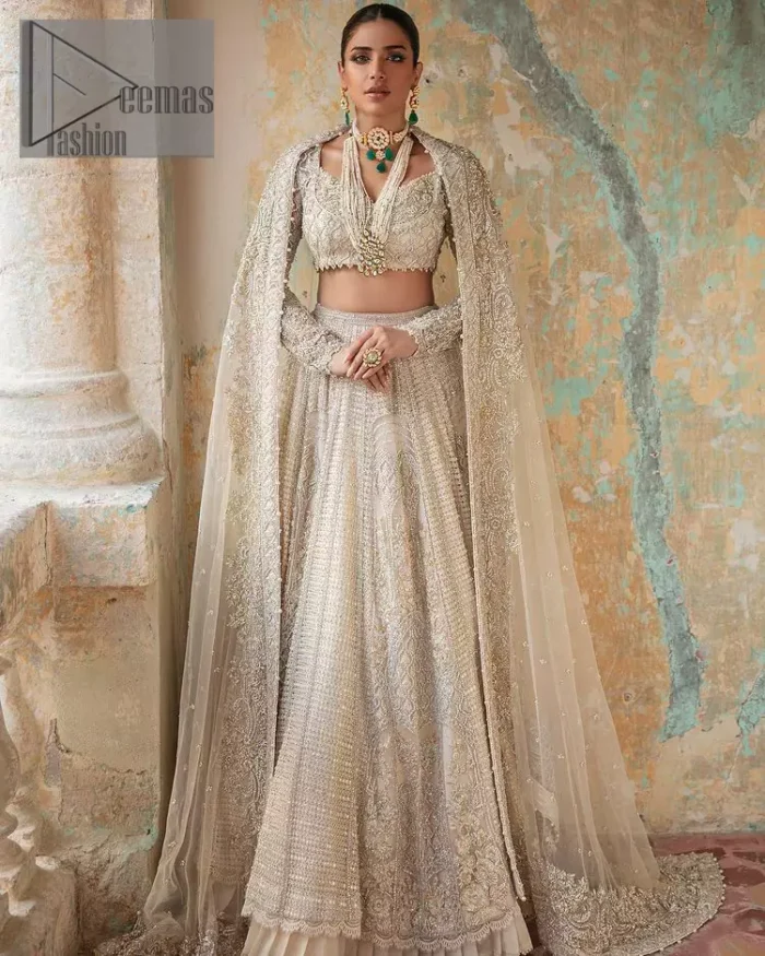 With a touch of Divine. A stunning ivory blouse is laboriously frosted with meticulously detailed hand embellishment with kora, dabka, tilla and pearls all over. The sweetheart neckline of the blouse and full sleeves together gives a so romantic look to any bride. In addition to this, it is systemized with the same colour frilled lehenga which is laden with the same colour embroidery that gives a magical stream of tilla, dabka and pearls. Finish this ivory article with the same colour dupatta that is heavily embellished with four-sided handsome borders and sequins sprayed all over to enhance the feeling of joy. 