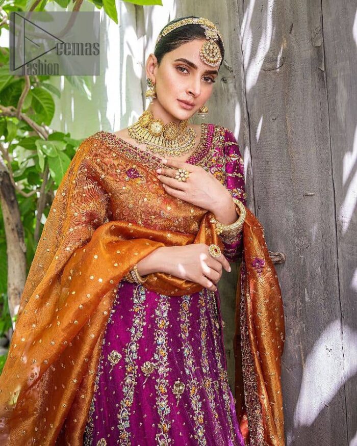 The outfit defines the true essence of allure with its spellbinding magenta hue and intricate details. The blouse is decorated with golden embroidery based on the neckline and sleeves. The sleeves are further enhanced with the embellished handwork. It is Beautifully organized with a magenta lehenga that is again heavily embellished with golden embroidery that is just adding poise to the whole look. Paired along with an orange dupatta decorated with subtly adorned motifs and embellished border that is completing this Mehandi looks wondrously.