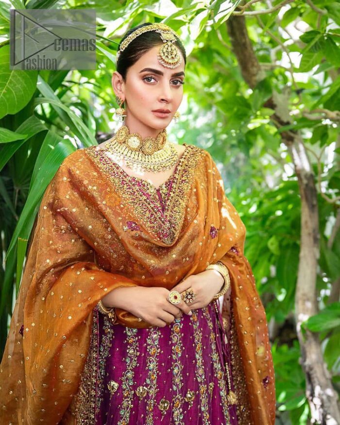 The outfit defines the true essence of allure with its spellbinding magenta hue and intricate details. The blouse is decorated with golden embroidery based on the neckline and sleeves. The sleeves are further enhanced with the embellished handwork. It is Beautifully organized with a magenta lehenga that is again heavily embellished with golden embroidery that is just adding poise to the whole look. Paired along with an orange dupatta decorated with subtly adorned motifs and embellished border that is completing this Mehandi looks wondrously.