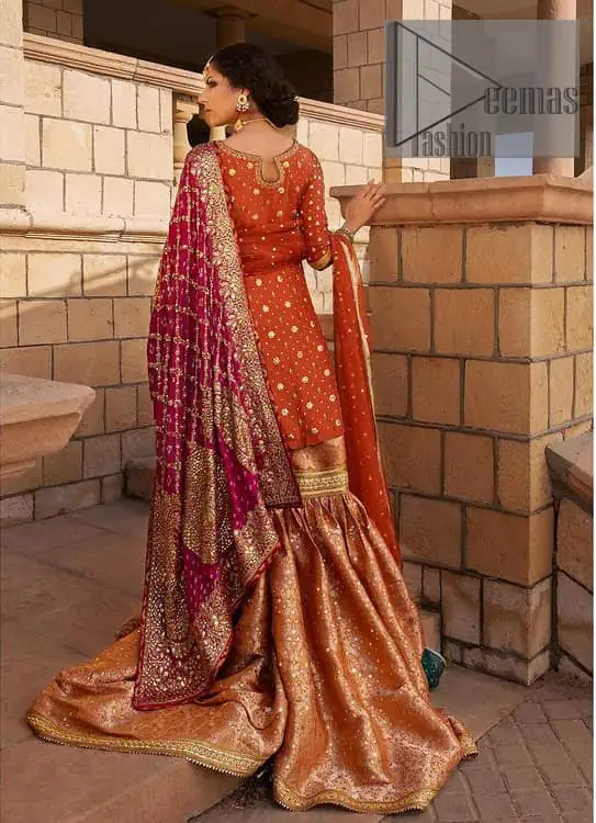 Be a happy and charming bride just like orange is a happy colour. DeemasFashion presents you with an orange short shit that is laboriously embellished with golden embroidery. The base of embroidery starts from the boat shape neckline of the shirt that giving a fully artistic look. In addition to this, it is enhanced with tilla, dabka, kora and Kundan work. The half sleeves of the dhirt also enhance the beauty of the handwork. It is coordinated with orange gharara that is perfect for entimate evening of your Mehandi. Finish this outfit with Pink dupatta that is adorned with ravishing details, the embellished borders represent the craftsmanship of DeemasFashion.
