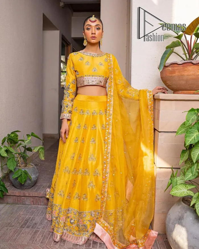 Yellow is just associated with mehndi as the sun is associated with brightness. DeemsFashion presents the bright yellow Pakistani mehndi outfit which laboriously begins with a blouse which is handsomely hand-rendered with silver and copper embroidery to make your day super duper bright. The boat shape neckline and full sleeves of this Pakistani mehndi outfit add to the breathtaking dream of the bride. It is paired up with a lehenga in the same colours which is adorned with floral motifs and bordered embroidery as well. Complete this Pakistani mehndi outfit with a dupatta in the same colour which is adorned with a four-sided embellished border and sequins sprayed all over.