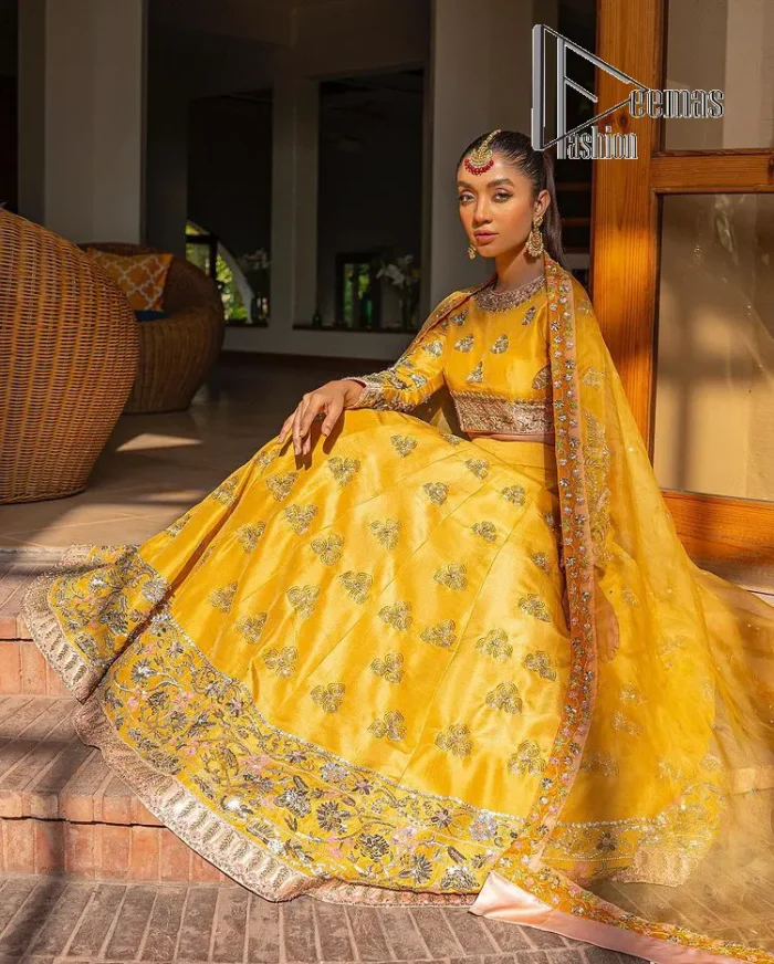Yellow is just associated with mehndi as the sun is associated with brightness. DeemsFashion presents the bright yellow Pakistani mehndi outfit which laboriously begins with a blouse which is handsomely hand-rendered with silver and copper embroidery to make your day super duper bright. The boat shape neckline and full sleeves of this Pakistani mehndi outfit add to the breathtaking dream of the bride. It is paired up with a lehenga in the same colours which is adorned with floral motifs and bordered embroidery as well. Complete this Pakistani mehndi outfit with a dupatta in the same colour which is adorned with a four-sided embellished border and sequins sprayed all over.