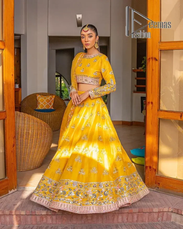 Yellow is just associated with mehndi as the sun is associated with brightness. DeemsFashion presents the bright yellow Pakistani mehndi outfit which laboriously begins with a blouse which is handsomely hand-rendered with silver and copper embroidery to make your day super duper bright. The boat shape neckline and full sleeves of this Pakistani mehndi outfit add to the breathtaking dream of the bride. It is paired up with a lehenga in the same colours which is adorned with floral motifs and bordered embroidery as well. Complete this Pakistani mehndi outfit with a dupatta in the same colour which is adorned with a four-sided embellished border and sequins sprayed all over.