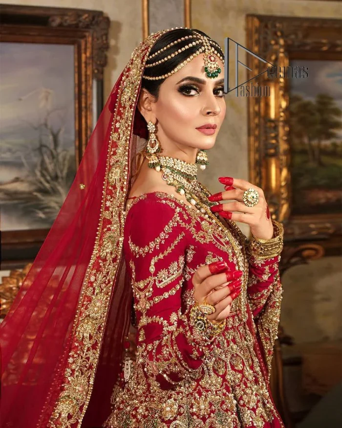 Happiness and confidence are the prettiest things that are associated with your wedding outfit. DeemasFashion presents this Pakistani reception wear in deep red colour. The deep red heavy maxi of this Pakistani reception wear is gorgeously adorned with a golden embroidery which is further enhanced with tilla, dabka, and kora. The boat shape neckline speaks of the boldness of the outfit. The following maxi is paired up with maroon sharara whose border is also embellished. Out and out of this Pakistani reception wears a dupatta in the same colour which is adorned with a four-sided border. Further, it is decorated with sequins sprayed all over.