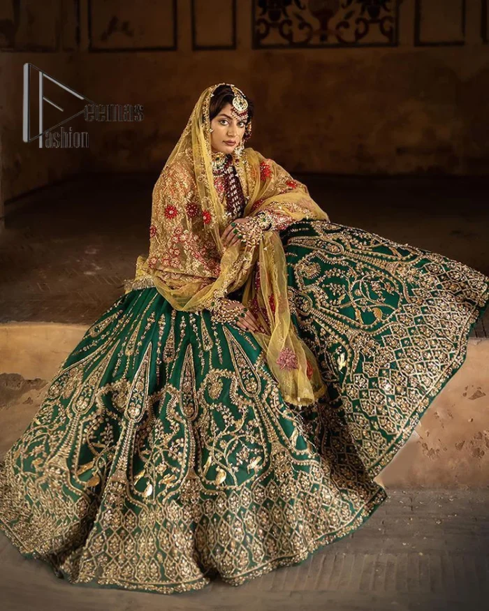 The blushing moment you found your dream mehndi outfit. This mehndi outfit is handsomely and attractively prepared in the level of contrast. Starting this mehndi outfit with a red blouse which is laboriously hand-rendered with light golden embroidery having tilla, kora, dabka and zardozi. In addition to this, it is enhanced with full sleeves and boat shape neckline to make your day super blush. The mehndi outfit is coordinated with a bottle green lehenga which is heavily ornamented with golden embroidery. Complete this article with a golden dupatta having Kiran on all sides. 