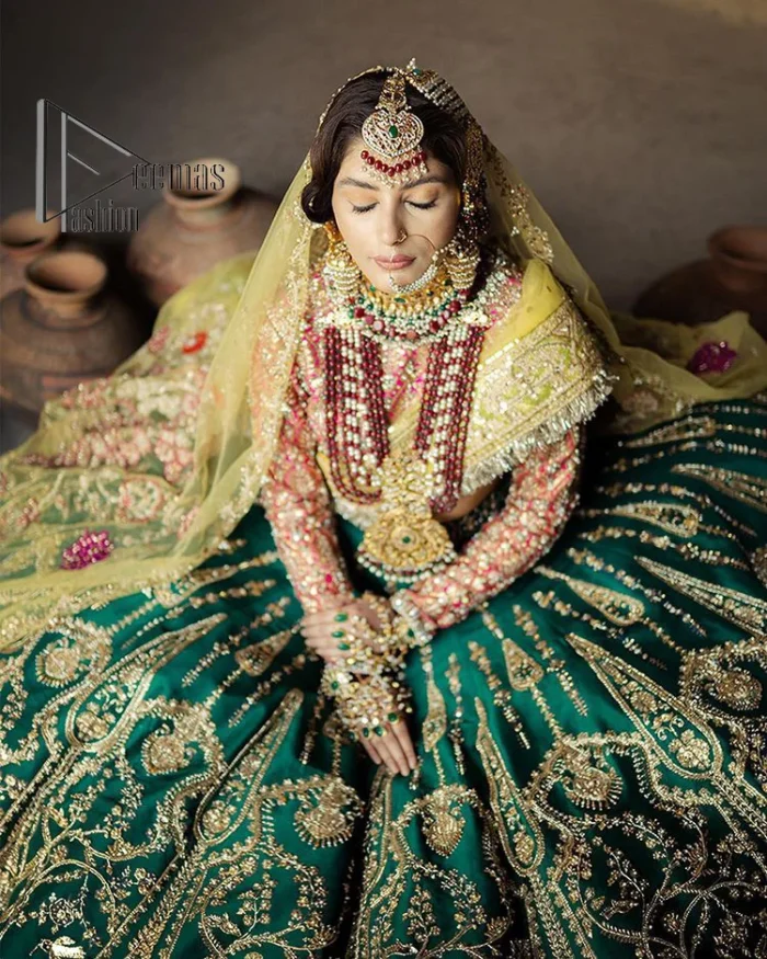 The blushing moment you found your dream mehndi outfit. This mehndi outfit is handsomely and attractively prepared in the level of contrast. Starting this mehndi outfit with a red blouse which is laboriously hand-rendered with light golden embroidery having tilla, kora, dabka and zardozi. In addition to this, it is enhanced with full sleeves and boat shape neckline to make your day super blush. The mehndi outfit is coordinated with a bottle green lehenga which is heavily ornamented with golden embroidery. Complete this article with a golden dupatta having Kiran on all sides. 