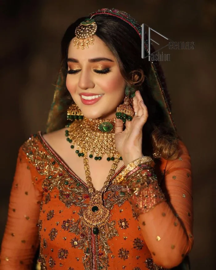 A colourful mehndi outfit is a power which directly influences the soul. Begin this mehndi outfit with a rusted front open shirt which is beautifully decorated with colourful embroidery to give you more power on your mehndi day. It is prominent with tilla, dabka, kora and zardozi. Further, the V shape neckline adds to this mehndi outfit when comes with full sleeves. Paired with a green lehenga having multiple colour borders to give you a more traditional look also. Complete this mehndi outfit with a colourful dupatta which is adorned with four-sided borders and sequins sprayed all over.
