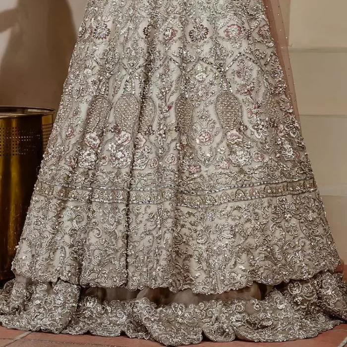 Walk with style on your Nikah day and let the flare follow! This light fawn flare maxi is decorated with tilla, dabka, kora, Kundan and details of Zardozi and enhanced with light golden embroidery for a unique artistic look. Further, the boat shape neckline also intensified the beauty of the outfit when comes with full sleeves. It is coordinated with flare lehenga in the same colour having border embellished to make your day booster day. Complete this outfit with a dupatta, framed with a four sided embellished border and sequins sprayed all over.