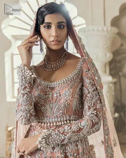 Steal the spotlight at your walima with this light orange yet subtle ensemble! This blouse is in a beautiful shade of orange and is deftly adorned with glowing tilla, dabka and pearls making this ensemble truly ethereal and incandescent. It enhances with the incrusted silver embroidery to make your day. Further, the round neckline of the blouse gives a romantic look when comes with full sleeves. The following blouse is coordinated with a floor-length lehenga which is heavily adorned. The flare of the lehenga adds super beauty to this marvellous masterpiece. Complete this article with a dupatta, framed with a four-sided border and tiny floral motifs all over to steal the spotlight of the show.