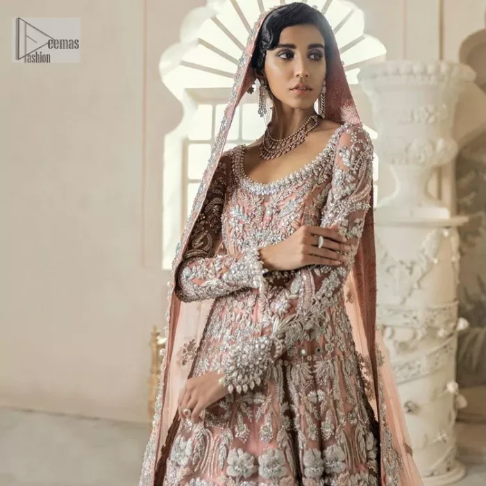 Steal the spotlight at your walima with this light orange yet subtle ensemble! This blouse is in a beautiful shade of orange and is deftly adorned with glowing tilla, dabka and pearls making this ensemble truly ethereal and incandescent. It enhances with the incrusted silver embroidery to make your day. Further, the round neckline of the blouse gives a romantic look when comes with full sleeves. The following blouse is coordinated with a floor-length lehenga which is heavily adorned. The flare of the lehenga adds super beauty to this marvellous masterpiece. Complete this article with a dupatta, framed with a four-sided border and tiny floral motifs all over to steal the spotlight of the show.