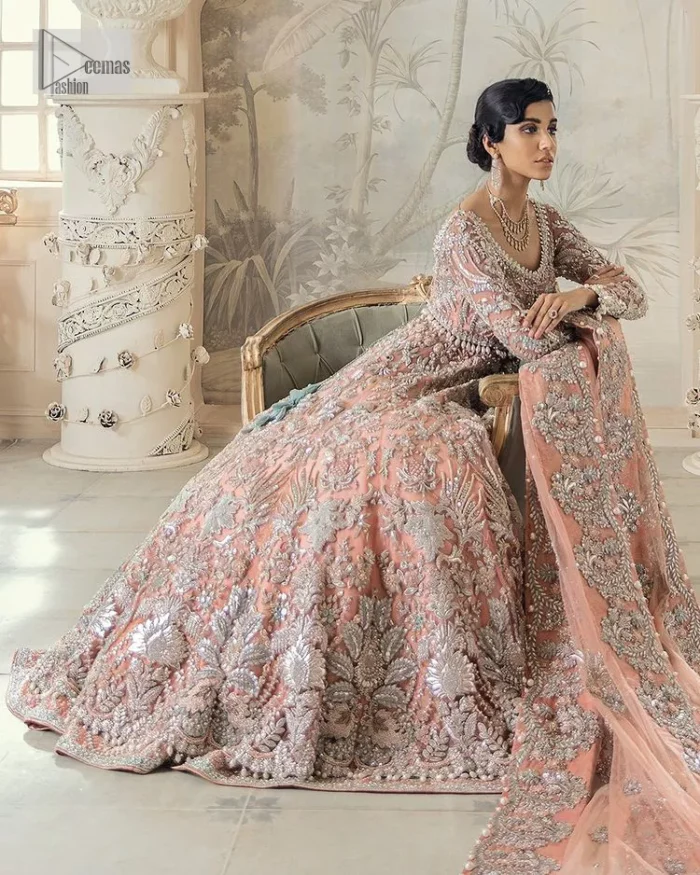 Steal the spotlight at your walima with this light orange yet subtle ensemble! This blouse is in a beautiful shade of orange and is deftly adorned with glowing tilla, dabka and pearls making this ensemble truly ethereal and incandescent. It enhances with the incrusted silver embroidery to make your day. Further, the round neckline of the blouse gives a romantic look when comes with full sleeves. The following blouse is coordinated with a floor-length lehenga which is heavily adorned. The flare of the lehenga adds super beauty to this marvellous masterpiece. Complete this article with a dupatta, framed with a four-sided border and tiny floral motifs all over to steal the spotlight of the show.