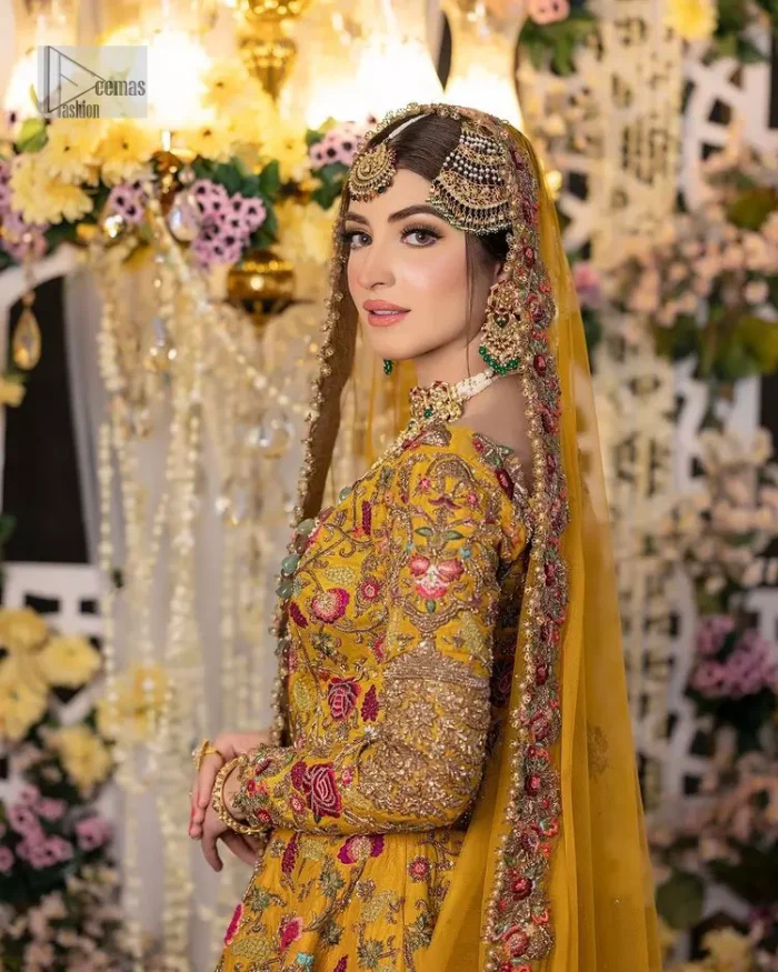 Take your style quotient up a few notches in this exquisite mehndi outfit! ]The maxi in mustard colour is a ravishing bridal attire with a magnificent elite and classy appearance. Gorgeous and glamorous multiple-colour embroideries enhance the showiness of this maxi.  It is further intensified with tilla, dabka, kora, Kundan and details of thread embroidery. Full sleeves, boat shape neckline and sparkling work make it a perfect traditional wear. It is coordinated with a scalloped dupatta in the same colour which is embellished with four-sided borders and floral motifs all over to make this outfit unique and aesthetic.