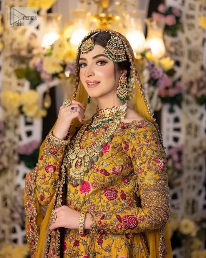Take your style quotient up a few notches in this exquisite mehndi outfit! ]The maxi in mustard colour is a ravishing bridal attire with a magnificent elite and classy appearance. Gorgeous and glamorous multiple-colour embroideries enhance the showiness of this maxi.  It is further intensified with tilla, dabka, kora, Kundan and details of thread embroidery. Full sleeves, boat shape neckline and sparkling work make it a perfect traditional wear. It is coordinated with a scalloped dupatta in the same colour which is embellished with four-sided borders and floral motifs all over to make this outfit unique and aesthetic.