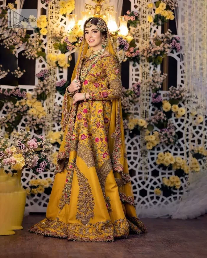 Take your style quotient up a few notches in this exquisite mehndi outfit! ]The maxi in mustard colour is a ravishing bridal attire with a magnificent elite and classy appearance. Gorgeous and glamorous multiple-colour embroideries enhance the showiness of this maxi.  It is further intensified with tilla, dabka, kora, Kundan and details of thread embroidery. Full sleeves, boat shape neckline and sparkling work make it a perfect traditional wear. It is coordinated with a scalloped dupatta in the same colour which is embellished with four-sided borders and floral motifs all over to make this outfit unique and aesthetic.