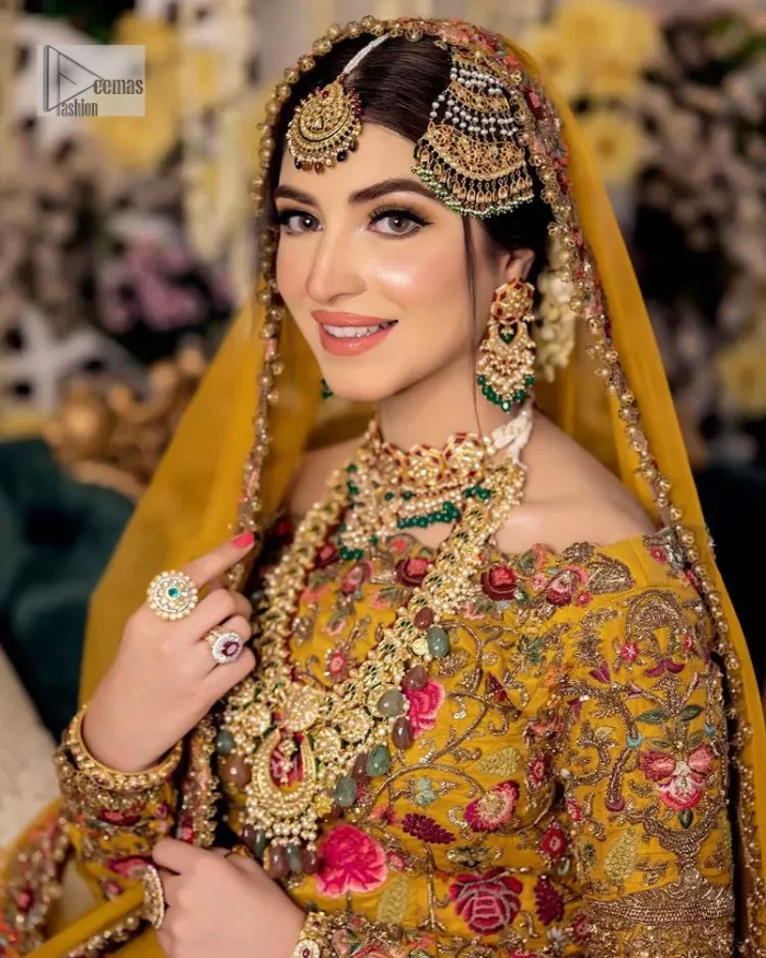 Take your style quotient up a few notches in this exquisite mehndi outfit! ]The maxi in mustard colour is a ravishing bridal attire with a magnificent elite and classy appearance. Gorgeous and glamorous multiple-colour embroideries enhance the showiness of this maxi.  It is further intensified with tilla, dabka, kora, Kundan and details of thread embroidery. Full sleeves, boat shape neckline and sparkling work make it a perfect traditional wear. It is coordinated with a scalloped dupatta in the same colour which is embellished with four-sided borders and floral motifs all over to make this outfit unique and aesthetic.