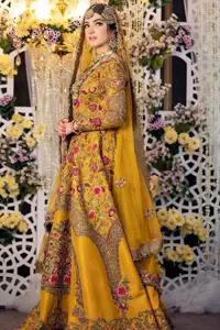 Take your style quotient up a few notches in this exquisite mehndi outfit! ]The maxi in mustard colour is a ravishing bridal attire with a magnificent elite and classy appearance. Gorgeous and glamorous multiple-colour embroideries enhance the showiness of this maxi.  It is further intensified with tilla, dabka, kora, Kundan and details of thread embroidery. Full sleeves, boat shape neckline and sparkling work make it a perfect traditional wear. It is coordinated with a scalloped dupatta in the same colour which is embellished with four-sided borders and floral motifs all over to make this outfit unique and aesthetic.