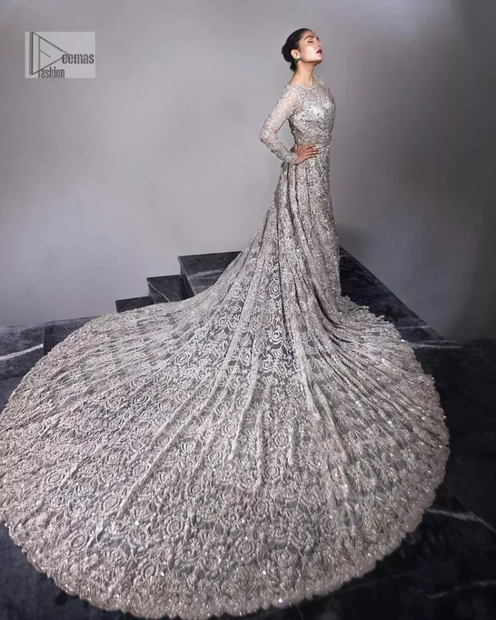 The trend of the back trains is still going strong as nikah wear - Here is the perfect one! This beautiful silver maxi is heavily embellished with silver embroidery. The gorgeous work of pearls, dabka, kora, Kundan and silver stones enhance the overall glamour of this maxi. The extraordinary design of the jewel neckline is completely embellished with silver stones and pearls embroidery combinations. The silver stones touch-up increases the looks of the beautiful gown with long tails that gives everlasting impact and at the bottom is the double flare. The full sleeves of the maxi are the lavishing style that any bride can wear on her big day.
