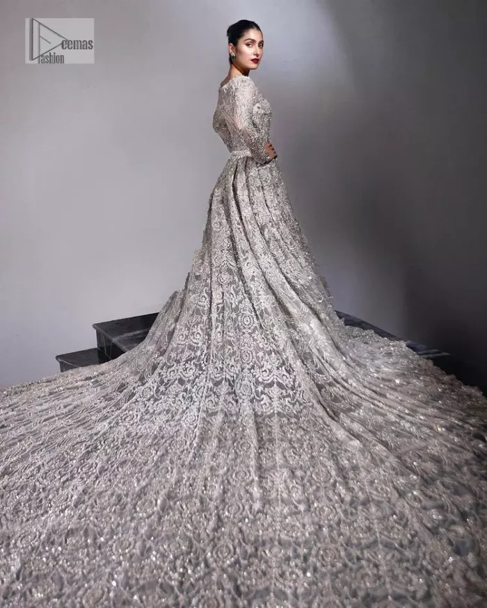 The trend of the back trains is still going strong as nikah wear - Here is the perfect one! This beautiful silver maxi is heavily embellished with silver embroidery. The gorgeous work of pearls, dabka, kora, Kundan and silver stones enhance the overall glamour of this maxi. The extraordinary design of the jewel neckline is completely embellished with silver stones and pearls embroidery combinations. The silver stones touch-up increases the looks of the beautiful gown with long tails that gives everlasting impact and at the bottom is the double flare. The full sleeves of the maxi are the lavishing style that any bride can wear on her big day.