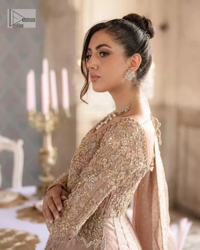 Make your Qabool Hai moment more memorable with this outfit by DeemasFashion. A dreamy statement of this dress proffers a soft pink hue with glamorous silver and golden embroidery.  It is further enhanced with tilla, dabka, kora, Kundan and the real magic of zardozi. V neckline enhances the overall glamour of this masterpiece. Intricate designs and fine details on the sleeves give a perfect finishing look to this maxi. The maxi is layered over a meticulously handcrafted lehnga which is bold enough to stand out in the crowd. Finish this article with a dupatta which is ornamented with four-sided borders and sequins sprayed all over which is a unique piece for your Nikah look. 