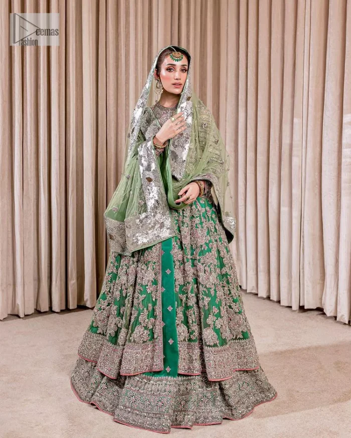 Dive into the world of ultimate allurement with this exquisitely embellished Mehndi outfit that depicts intricate glam with an elegant statement detailing. The maxi in teal green colour is heavily adorned with silver embroidery which involves tilla, dabka, kora, Kundan and the real magic of Zardozi. Further, the high neckline and full sleeves add extra glamour to this outfit. It is organized with magnificent lehenga in the same colour emblazoned with intricate gleaming embroidery which enhances the charm of this Dress. The tiny floral motifs also spread on the lehenga. Complete this article with a dupatta framed with four-sided borders and tiny floral motifs all over to make your day charming.