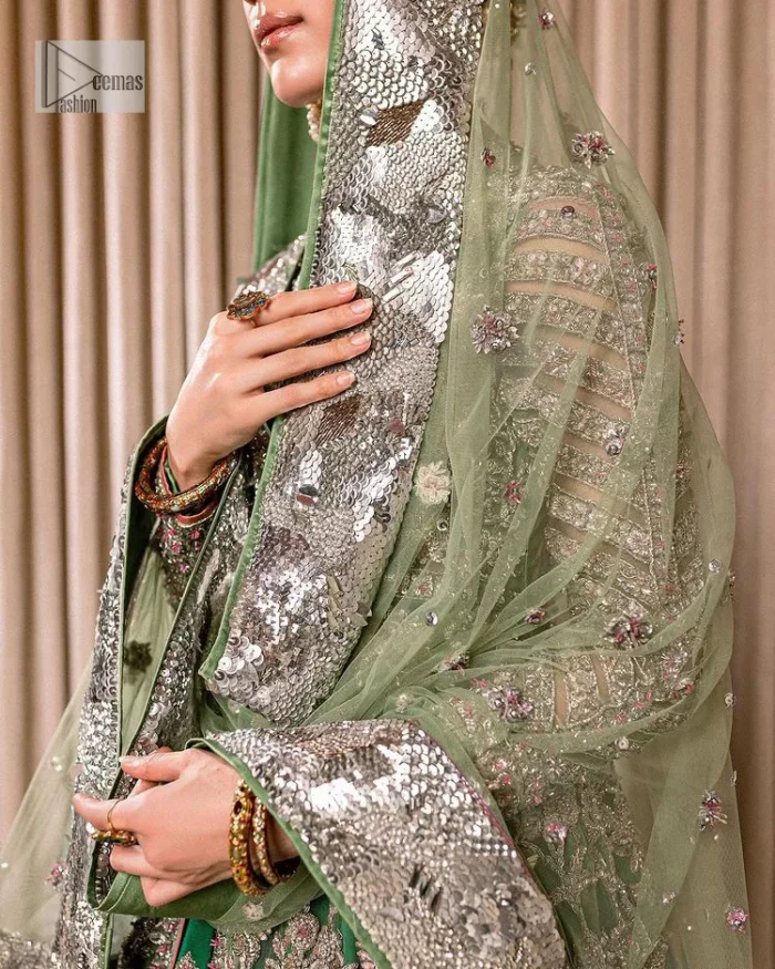 Dive into the world of ultimate allurement with this exquisitely embellished Mehndi outfit that depicts intricate glam with an elegant statement detailing. The maxi in teal green colour is heavily adorned with silver embroidery which involves tilla, dabka, kora, Kundan and the real magic of Zardozi. Further, the high neckline and full sleeves add extra glamour to this outfit. It is organized with magnificent lehenga in the same colour emblazoned with intricate gleaming embroidery which enhances the charm of this Dress. The tiny floral motifs also spread on the lehenga. Complete this article with a dupatta framed with four-sided borders and tiny floral motifs all over to make your day charming.