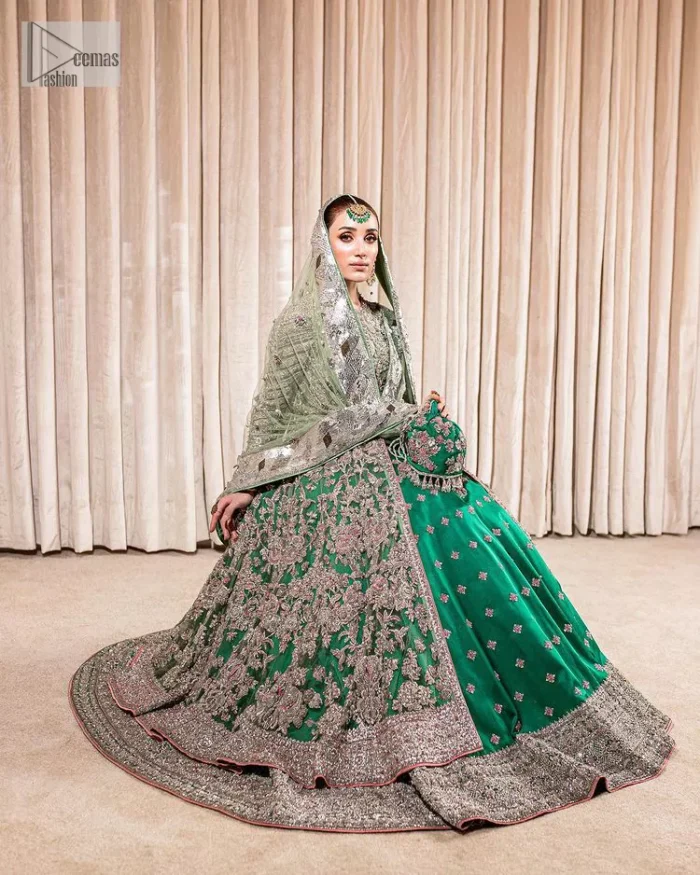 Dive into the world of ultimate allurement with this exquisitely embellished Mehndi outfit that depicts intricate glam with an elegant statement detailing. The maxi in teal green colour is heavily adorned with silver embroidery which involves tilla, dabka, kora, Kundan and the real magic of Zardozi. Further, the high neckline and full sleeves add extra glamour to this outfit. It is organized with magnificent lehenga in the same colour emblazoned with intricate gleaming embroidery which enhances the charm of this Dress. The tiny floral motifs also spread on the lehenga. Complete this article with a dupatta framed with four-sided borders and tiny floral motifs all over to make your day charming.