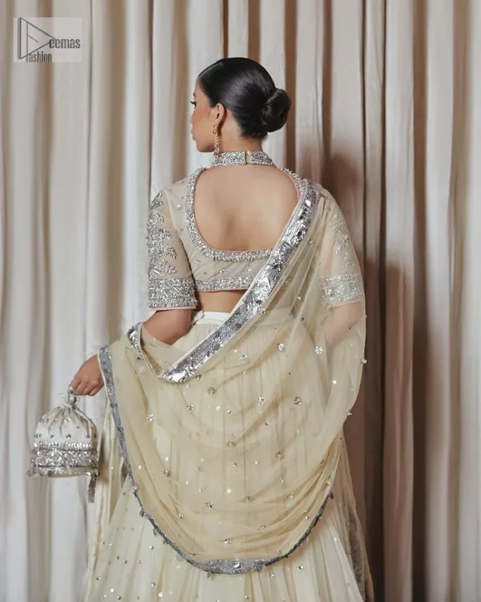 The perfect balance of simplicity and flamboyance is the essence of the beautiful Walima outfit. The blouse in off-white colour is beautifully embellished with Dabka, Tilla, Zardozi and delicate yet intricate crystal work. The beautiful classy artistic half sleeves design maintains the charm of this blouse. The beautiful outfit is epitome of beauty by its high neckline . It is paired up with flared lehenga in the same colour, framed with a sequins sprayed all over. Further, beautiful silver embroidery on the four sided border of the dupatta will enhance the overall magnificent look.