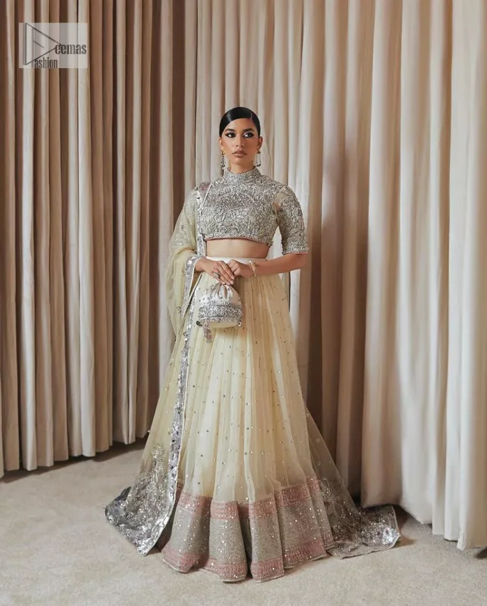 The perfect balance of simplicity and flamboyance is the essence of the beautiful Walima outfit. The blouse in off-white colour is beautifully embellished with Dabka, Tilla, Zardozi and delicate yet intricate crystal work. The beautiful classy artistic half sleeves design maintains the charm of this blouse. The beautiful outfit is epitome of beauty by its high neckline . It is paired up with flared lehenga in the same colour, framed with a sequins sprayed all over. Further, beautiful silver embroidery on the four sided border of the dupatta will enhance the overall magnificent look.