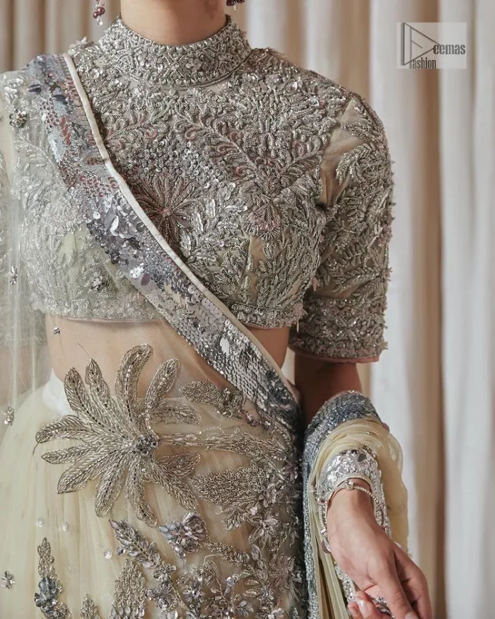 The perfect balance of simplicity and flamboyance is the essence of the beautiful Walima outfit. The blouse in off-white colour is beautifully embellished with Dabka, Tilla, Zardozi and delicate yet intricate crystal work. The beautiful classy artistic half sleeves design maintains the charm of this blouse. The beautiful outfit is epitome of beauty by its high neckline . It is paired up with flared lehenga in the same colour, framed with a sequins sprayed all over. Further, beautiful silver embroidery on the four sided border of the dupatta will enhance the overall magnificent look.