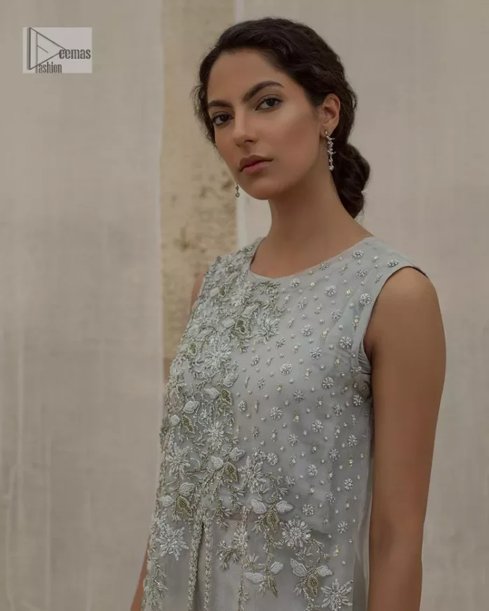 Balancing outfit lovers here’s your style treat! The handsome and charming steel grey attire is an epitome of elegance and royalty that gives you a head-turning appearance on the party occasion. The front open gown is laden with silver embroidery that is further enhanced with tilla, dabka, kora, Kundan and luxuries of crystals. The round neckline of this gown is emblazoned with luxury designs and embroidery. In addition to this, the sleeveless style makes this article a masterpiece. Paired up with straight trousers to balance the look of this exquisite article.