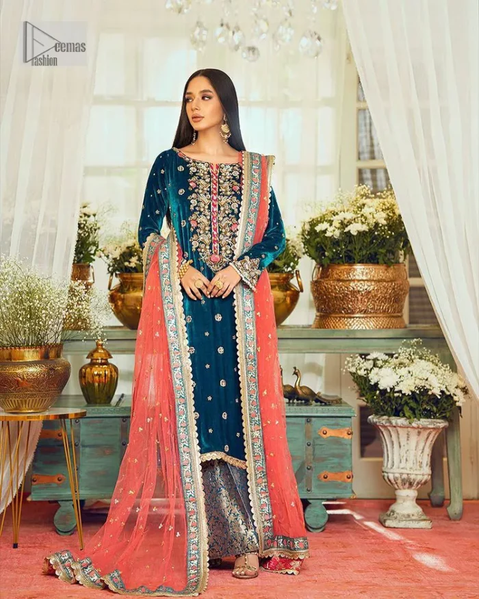 This dazzling yet elegant ensemble is perfect to make a statement at any event.  Long shirt for party dress in teal blue colour is embellished with multiple colour embroidery which is prominent with dabka, naqshi, stones, tilla, crystals work. The boat shape neckline is decorated with embroidery and with full-length sleeves. The fabric used for the shirt is velvet. It is paired with jamawar trousers in the same colour that is unique in style. Finish this party wear with a scalloped dupatta framed with a four-sided border and ting floral motifs all over that is the perfect choice for a party.