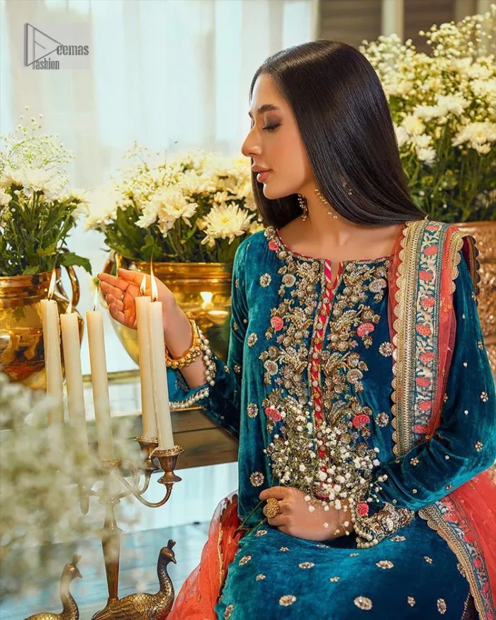 This dazzling yet elegant ensemble is perfect to make a statement at any event.  Long shirt for party dress in teal blue colour is embellished with multiple colour embroidery which is prominent with dabka, naqshi, stones, tilla, crystals work. The boat shape neckline is decorated with embroidery and with full-length sleeves. The fabric used for the shirt is velvet. It is paired with jamawar trousers in the same colour that is unique in style. Finish this party wear with a scalloped dupatta framed with a four-sided border and ting floral motifs all over that is the perfect choice for a party.