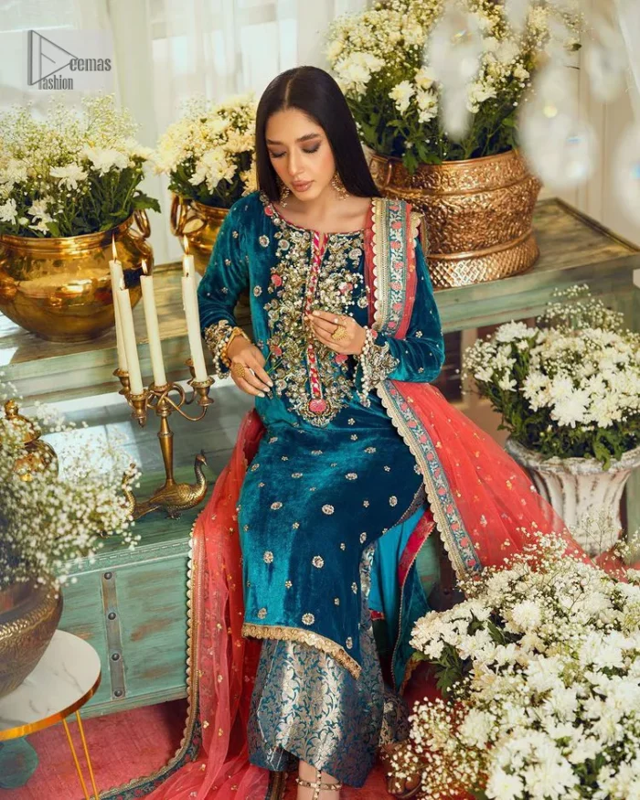 This dazzling yet elegant ensemble is perfect to make a statement at any event.  Long shirt for party dress in teal blue colour is embellished with multiple colour embroidery which is prominent with dabka, naqshi, stones, tilla, crystals work. The boat shape neckline is decorated with embroidery and with full-length sleeves. The fabric used for the shirt is velvet. It is paired with jamawar trousers in the same colour that is unique in style. Finish this party wear with a scalloped dupatta framed with a four-sided border and ting floral motifs all over that is the perfect choice for a party.