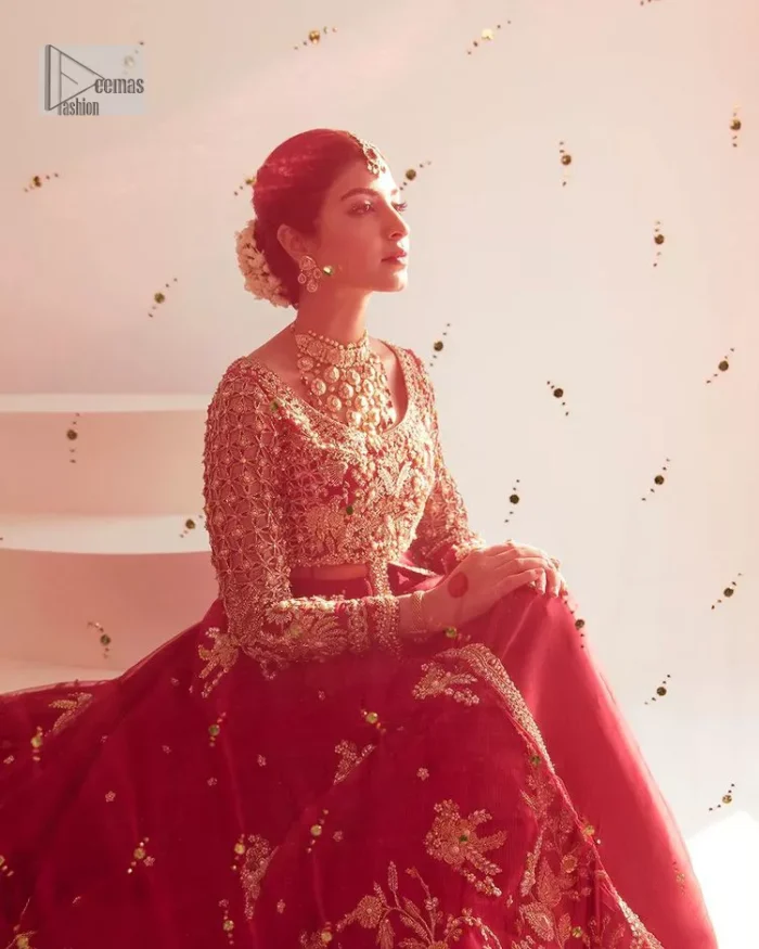 Be a dreamy vision in this reception wear. The beautiful pishwas in the bright red shade is embellished with intricate designs and fine details. It is enhanced with hand-crafted golden embroidery with details of tilla, dabka, kora, Kundan and magic of Zardozi. The round neckline and three-quarter sleeves feature a heavily crafted geometric pattern enhanced by cutwork detailing. The following front open scalloped pishwas is organized with a back train lehenga whose border is beautifully decorated with embroidery making it an epitome of beauty and grace. Furthermore, The embellished borders of the red scalloped dupatta give a perfectly glamorous look to the beautiful overall outfit. It is also intensified with sequins spray.