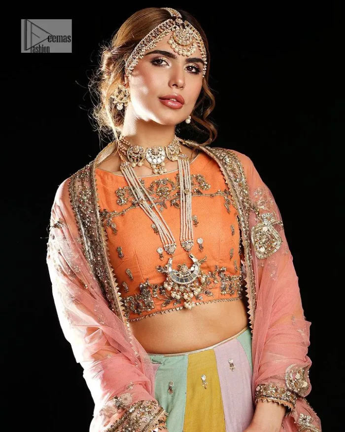 Fun colours, fresh you.  This breathtaking blouse in light orange colour is gracefully adorned with hand-crafted embellishments and lavish golden work creating a magnificent masterpiece to give you your desired appearance. The boat shape neckline of the mehndi wear is the epitome of beauty. Further, the embellished three-quarter is adorned with lavish designs and fine details making it a perfect choice to pair with the lehenga. It is organized with lehenga having multi-colour panels to give you a fresh and rainbow look on your mehndi. The lehenga is also adorned with tilla, dabka, kora, Kundan and the real magic of Zardozi. Complete this article with a dupatta, framed with four-sided borders and floral motifs on pallu to make your day Funday.