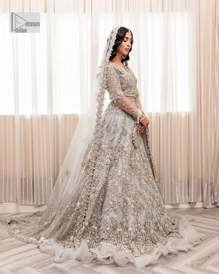Enter the world of allurement with steel grey, a gorgeous go-to dress for nikah to make you look classy and fabulous at the same time! The delicate details of this gorgeous bridal dress are from exquisite patterns observed in silver embroidery which is prominent with tilla, dabka, kora, Kundan, Zardozi and the real magic of crystals. The house has V shape neckline to make this masterpiece a little romantic and classy. Further, full sleeves are fully designed with fantastic floral patterns spread all over. It is paired with a lehenga having frilled to complete the lavish look of this fully embellished nikah wear. Complete this article with a dupatta adorned with four-sided embellished borders and sequins sprayed all over.