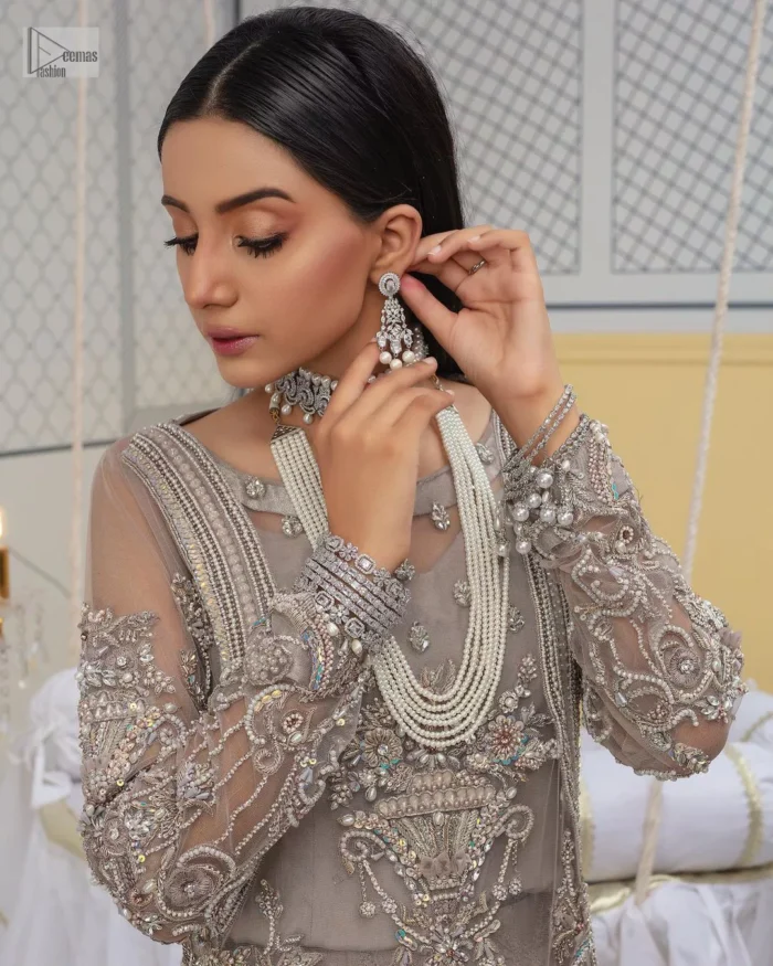 Chill vibes in grey are very rare. A beautiful grey shirt with a medley of hand-embellished floral motifs and floral patterns of silver embroidery which is highlighted with tilla, dabka, kora, Kundan and the real magic of Zardozi. The illusion neckline makes this party outfit a little romantic. Further, the floral patterns on full sleeves also add super beauty. It is paired up with plain jamawar trousers just to balance the look   Complete this gorgeous outfit with a dupatta in the same colour framed with four-sided borders and sequins sprayed all over. 