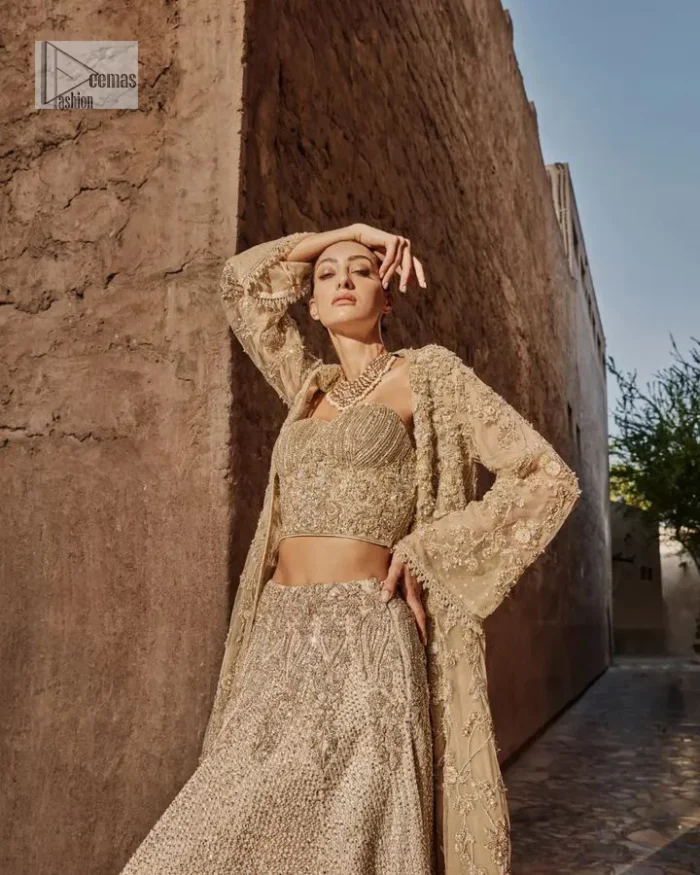 This modern piece is all about extraordinary details and aesthetic vibes! A beige organza blouse is heavily embellished with dabka, naqshi, tilla, Resham, dabka, sequin and Kundan. This gown blouse dress has Mughal-inspired motifs, geometrical patterns and floral motifs. The blouse has a sweetheart neckline or a more upscale appearance and feel. Further, the gown has full sleeves adorned with floral patterns. It is supported by a flared lehenga with an embellished border for additional comfort.