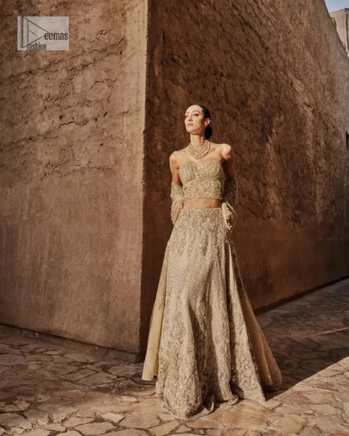 This modern piece is all about extraordinary details and aesthetic vibes! A beige organza blouse is heavily embellished with dabka, naqshi, tilla, Resham, dabka, sequin and Kundan. This gown blouse dress has Mughal-inspired motifs, geometrical patterns and floral motifs. The blouse has a sweetheart neckline or a more upscale appearance and feel. Further, the gown has full sleeves adorned with floral patterns. It is supported by a flared lehenga with an embellished border for additional comfort.
