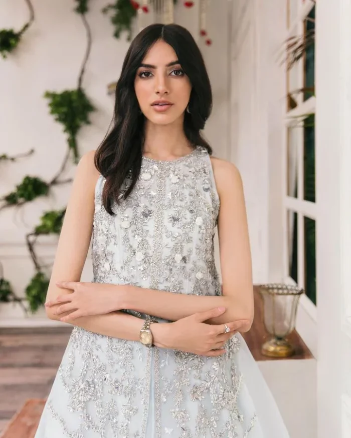 Shine and sparkle in this ice-blue nikah outfit! A mesmerizing long shirt stuns in a beautifully handcrafted silver embroidery enshrined with tilla,dabka, kora, Kundan, Zardozi, stones and the real magic of crystals. The jewel neckline has detailed intricate floral patterns. The sleeveless style of this ice blue front open shirt is the true essence of DeemasFashion. It is organized with a plain lehenga in the same colour to complete your stylish appearance.