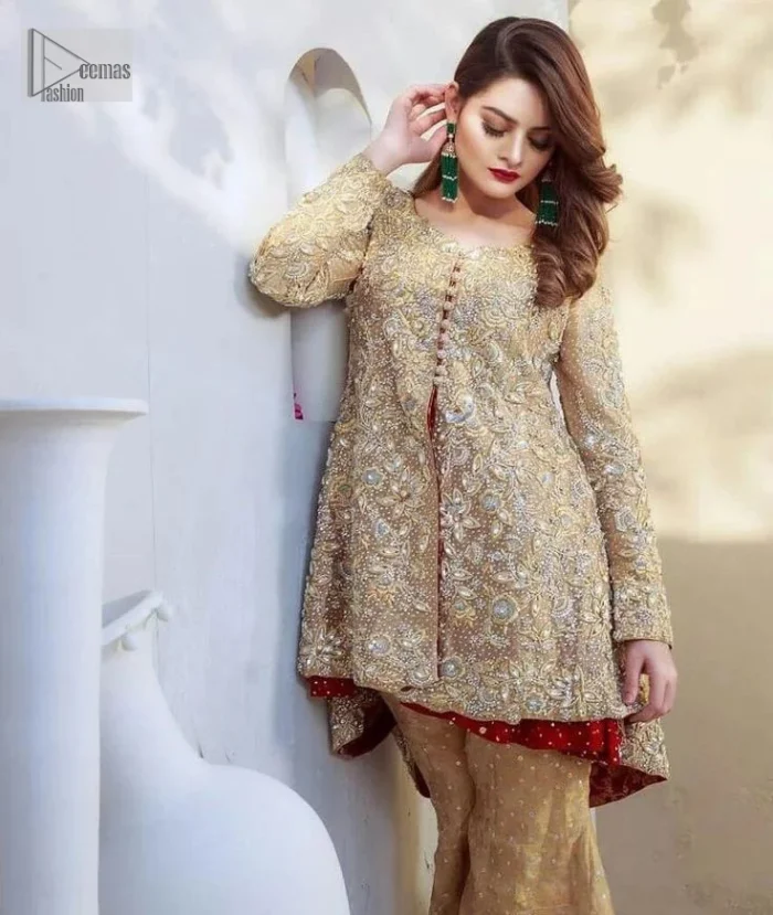 Clean, modern and timeless. The beautiful front-open short shirt in a light golden colour is adorned with embellishments of silver embroidery. It is enhanced with tilla, dabka, kora, Kundan and the real magic of Zardozi. The round neckline makes this outfit unique and lovely. Further, the floral patterns on full sleeves also add super beauty to the outfit. The inner of the short shirt has a red frock combination that gives an aesthetic look. Complete this article with trousers in the same colour as a short shirt just to balance the royal look.   