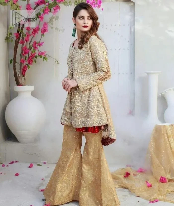 Clean, modern and timeless. The beautiful front-open short shirt in a light golden colour is adorned with embellishments of silver embroidery. It is enhanced with tilla, dabka, kora, Kundan and the real magic of Zardozi. The round neckline makes this outfit unique and lovely. Further, the floral patterns on full sleeves also add super beauty to the outfit. The inner of the short shirt has a red frock combination that gives an aesthetic look. Complete this article with trousers in the same colour as a short shirt just to balance the royal look.   