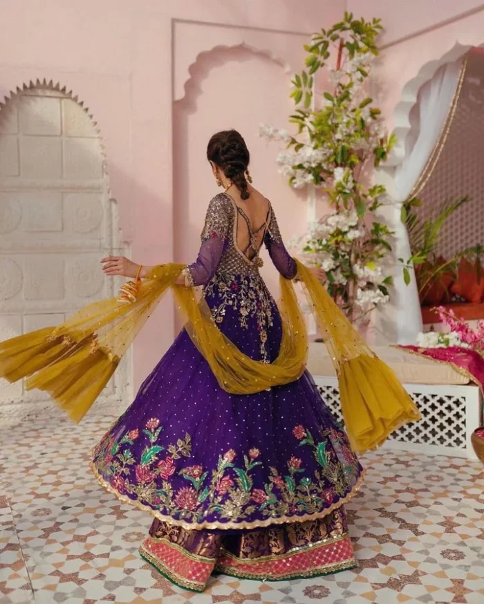 Slay your mehndi looks with signature statement pieces. This stunning plum frock is gracefully emblazoned with tilla, dabka, kora, Kundan, Zardozi and crystal details and graceful multiple-colour embroidery work giving you a breathtaking dreamy appearance at the wedding. The floral motifs on the three-quarter sleeves add grace to the outfit. Further, the round neckline has fine details. It is paired up with a lehenga in the same colour having prominent borders just to prominent you on your Mehndi day. Complete this mehndi outfit with a dupatta with sparkling sequins all over to slay your look.
