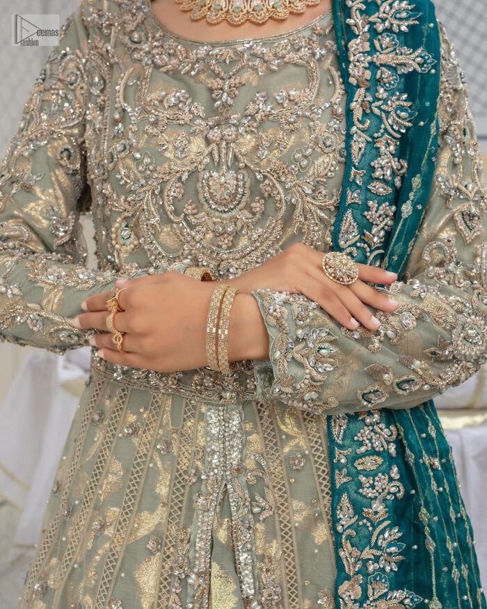 Embellishment is on the rise! The elegant front open maxi is heavily embellished in work of tilla, sequins, dabka, Zardozi, Kundan and kora work. The magnificent maxi is further highlighted with silver embroidery on the front and backside. Further, the full sleeves of the dress come with attractive embellishments. The round neckline makes this masterpiece more unique and charming. This nikah outfit is coordinated with a dupatta in teal green colour framed with a four-sided border and sparkling sequins all over that are on the peak in modern style.