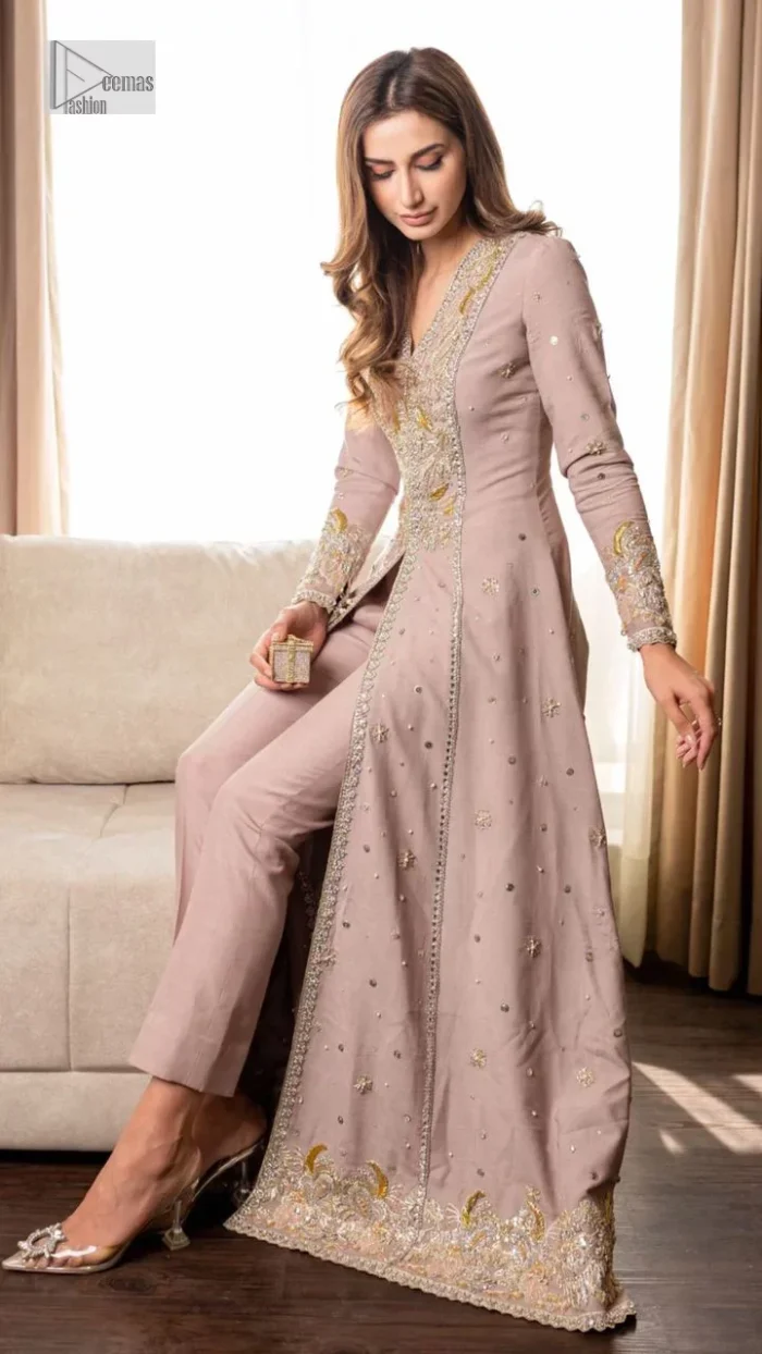 Feel the magic of the party in this splendid article! The ideal front open gown in tea rose colour is heavily hand embellished with floral branches and botanical motifs. It has an embroidered border on the front and back. The V shape neckline is adorned with silver and golden embroidery. It is further prominent with tilla,dabka, kora, Kundan, crystals, stones and the intricate detailing of Zardozi to make this masterpiece lovely and charming. Further, the full sleeves are decorated with tiny floral motifs and sequins spray. It is paired with trousers that complete the party wear look.