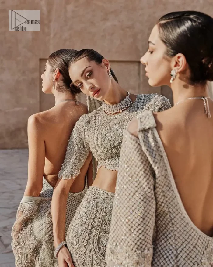 This fusion of floral embroidery is total fashion goodness for a walima outfit! A stunning teal grey organza choli embellished with intricate detailing finished with a scalloped border. The beautiful blouse is decorated with silver embellishment which is further prominent with tilla,daka, kora, Kundan and the real magic of Zardozi.  It is paired with a heavily embellished back-train lehenga with botanical motifs and geometric patterns. Its dupatta is made from a net. The dupatta is a wide embellished border that added divine charm to the entire ensemble.