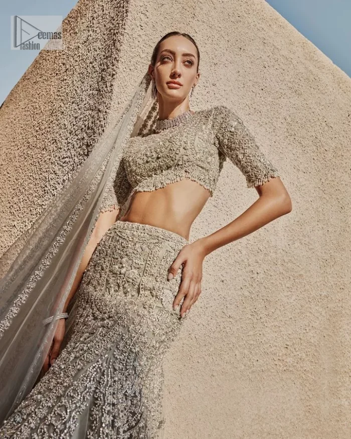 This fusion of floral embroidery is total fashion goodness for a walima outfit! A stunning teal grey organza choli embellished with intricate detailing finished with a scalloped border. The beautiful blouse is decorated with silver embellishment which is further prominent with tilla,daka, kora, Kundan and the real magic of Zardozi.  It is paired with a heavily embellished back-train lehenga with botanical motifs and geometric patterns. Its dupatta is made from a net. The dupatta is a wide embellished border that added divine charm to the entire ensemble.