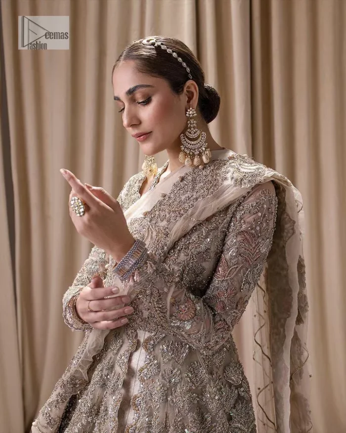 Make a statement with a light fawn article on your nikah day! DeemasFashion presents the light fawn heavy maxi which is embellished with silver embroidery using dabka, tilla, kora, Zardozi, Swarovski, Mukesh, sequin and Kundan. The strap neckline adds a little romanticness to the dress. Further, the floral patterns on full sleeves make this masterpiece modern and unique. It is paired with a  lehenga, embellished with a delicate border. It is styled with a dupatta; its surface is sprayed with sequin and the dupatta is enveloped by a heavily embellished floral border.